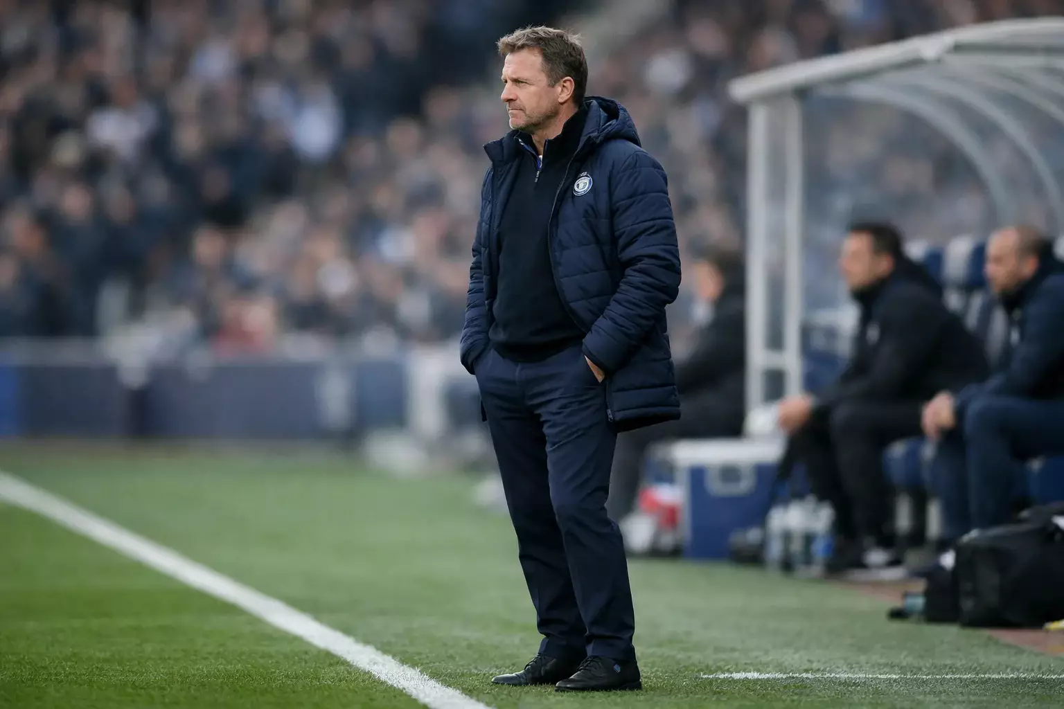Football manager standing on the touchline with a thoughtful expression during a match