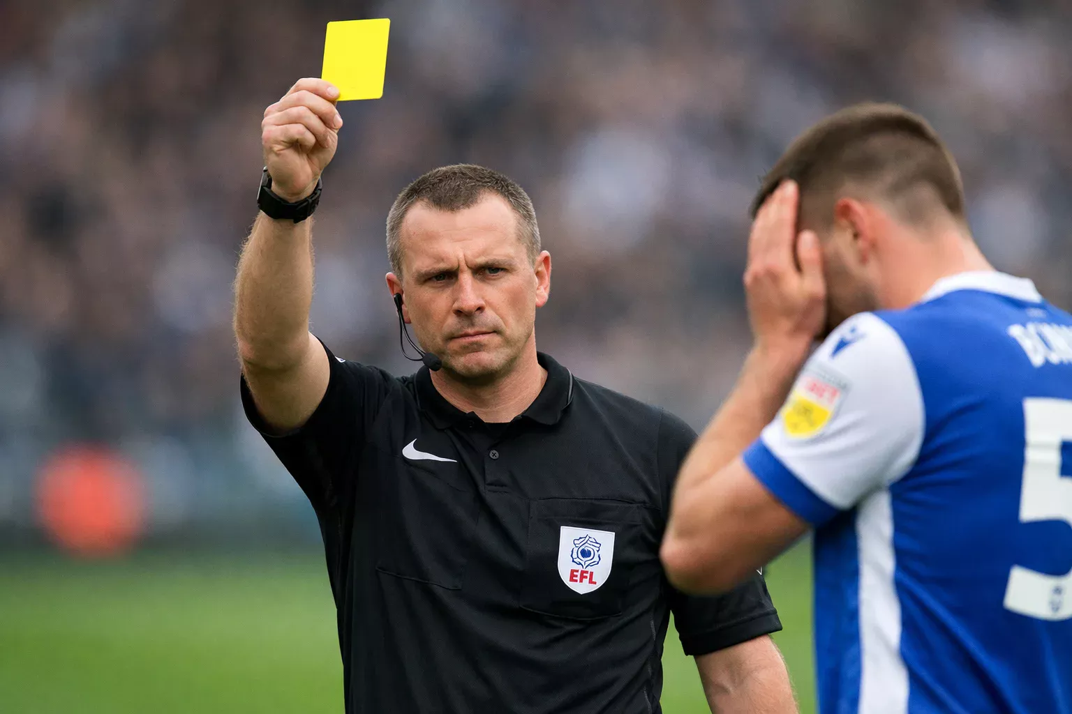 Football referee holding up a yellow card to a player during a match