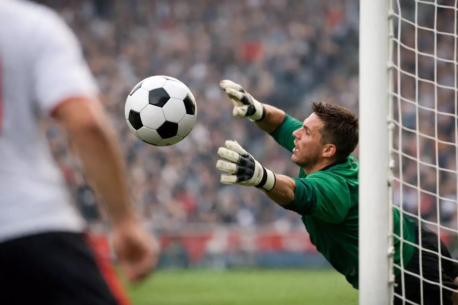 Football hitting the back of the net during a goal with goalkeeper diving